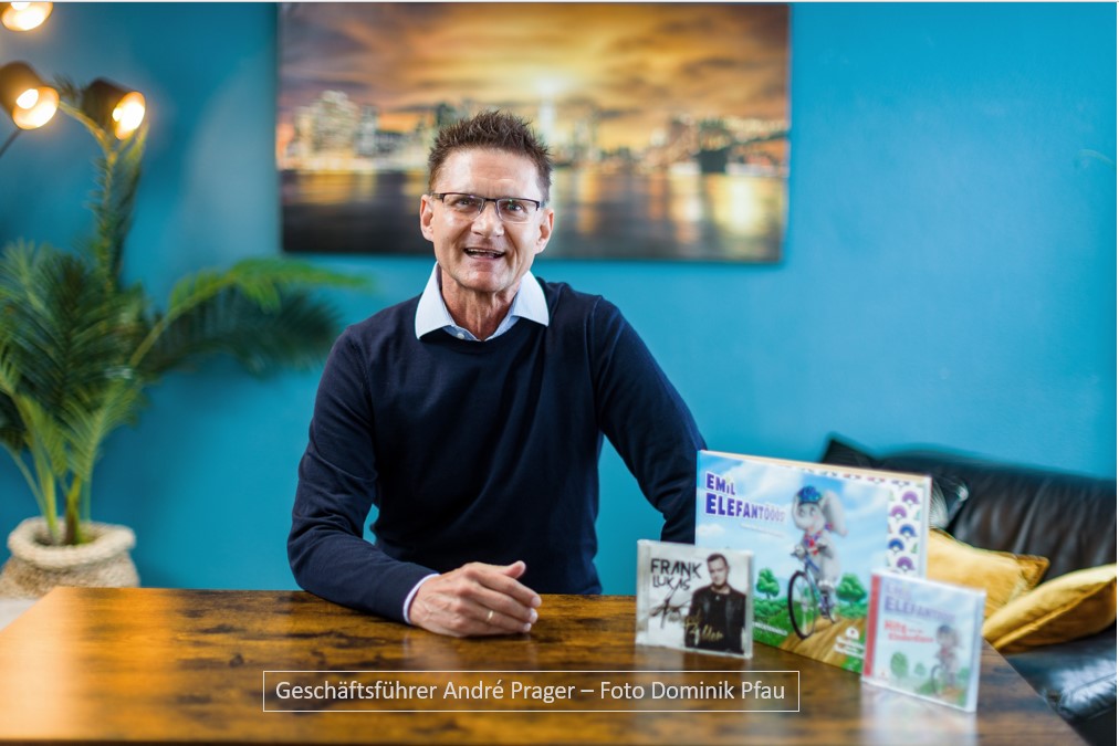 Foto Geschäftsführer André Prager inklusive Abbildung der Kooperationsprodukte Buch und CD "Emil Elefantööös" und der CD von Exklusivkünstler Frank Lukas "Tausend Bilder"